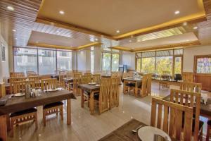 un restaurante con mesas y sillas de madera y ventanas en HOTEL WILD ROSE, en Jagatsukh