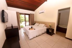 a bedroom with a white bed and a tub at Sun Bay Pipa Hotéis in Pipa