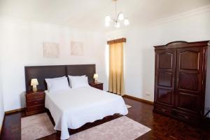 een slaapkamer met een wit bed en een houten kast bij Vivenda Glorizé in Água de Alto