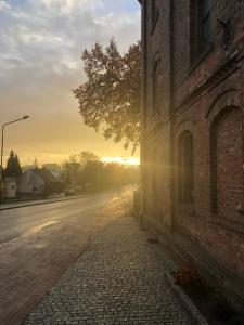 an empty street next to a brick building with the sun setting at Hotel Mały Młyn in Stargard