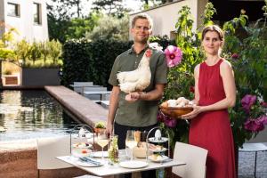 un hombre y una mujer sosteniendo un pollo de pie junto a una mesa en Gartenlofts auf Gut Guntrams en Schwarzau am Steinfelde