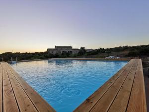 una piscina con bancos de madera frente a un edificio en B&B Al Tramonto Portopalo, en Portopalo di Capo Passero