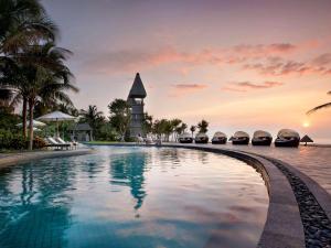 uma piscina no resort com uma torre de relógio ao fundo em Raffles Hainan Clear Water Bay em Sanya