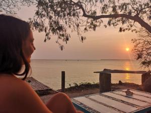 une femme assise sur une plage pour admirer le coucher du soleil dans l'établissement El Hamaquero Hostal EcoNativo, à Isla Grande