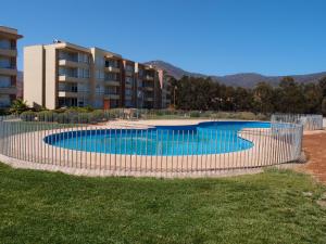 une piscine entourée d'une clôture en face d'un bâtiment dans l'établissement Acogedor Departamento en Balneario de Papudo-Condominio Lomas de Papudo 1 -Punta de Puyai, à Papudo