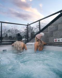 Dos mujeres están sentadas en un jacuzzi. en Basecamp Suites Canmore, en Canmore