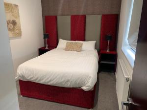 um pequeno quarto com uma cama com uma cabeceira vermelha em LuxuStay Serviced Apartments em Milton Keynes