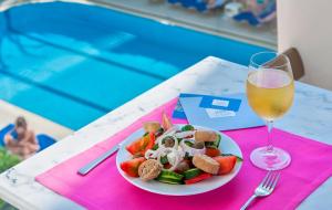 a plate of food and a glass of wine on a table at Ilios Beach Hotel Apartments ADULTS ONLY in Rethymno Town