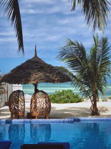 a pool with a straw umbrella and chairs next to a beach at Sofia Sea View in Pwani Mchangani