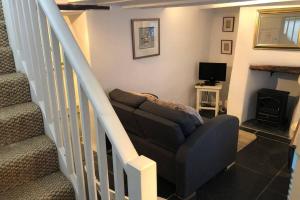 a living room with a couch and stairs with a television at Molls Yard Traditional Cottage in Port Isaac