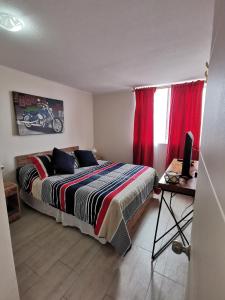 1 dormitorio con 1 cama con cortinas rojas y escritorio en Departamento en Avenida Del Mar, en La Serena