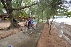 two people riding bikes on a sidewalk next to trees at Rocky Point Resort in Thap Sakae