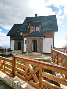 ein Haus mit einem schwarzen Dach und einem Holzzaun in der Unterkunft Vila Rajski kutak Kopaonik in Kopaonik