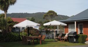 a patio with tables and umbrellas and a grill at Alpine Rose Motel in Greymouth