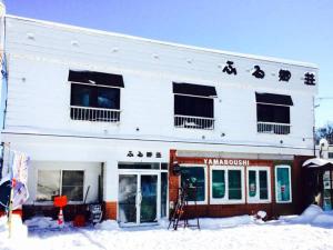 a white building with a store in the snow at ふる郷荘Furusato Furano in Furano