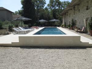 una piscina en un patio con sillas y sombrillas en Le Mas Vieux, en Graveson