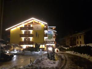 a yellow building with lights on it in the snow at Park Residence Imperator in Carisolo