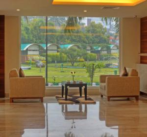 ein Wohnzimmer mit 2 Stühlen, einem Tisch und einem großen Fenster in der Unterkunft Hotel Le Ruchi The Prince in Mysore