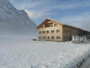 un bâtiment dans la neige à côté d'une montagne dans l'établissement Ferienwohnung Berchtold, à Schnepfau