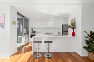 a white kitchen with a white counter and stools at Brand new house, amazing views, walk to the beach! in Kiama +18 photos