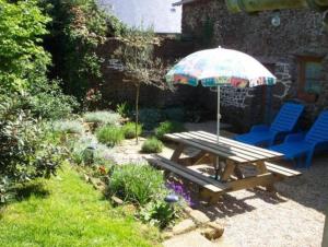 uma mesa de piquenique e cadeiras com um guarda-sol num jardim em Beautiful 3-Bed Cottage in Passais-Villages em Saint-Siméon
