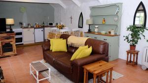 a living room with a brown couch and a kitchen at Cowshed Cottage located nr Kynance cove in Lizard