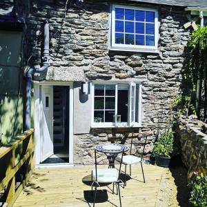 a table and chairs on a wooden deck in front of a stone house at Captivating Isolde Cottage with pool near St Ives in Camborne