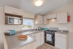 a kitchen with white cabinets and a black stove top oven at Stunning 6 Birth Caravan in Skegness Herons Mead in Orby