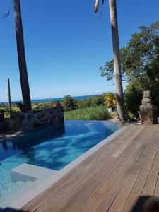 una piscina con una terraza de madera y palmeras en Villa de 2 chambres a Sainte Rose a 500 m de la plage avec vue sur la mer piscine privee et jardin clos, en Sainte-Rose