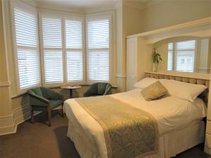 a bedroom with a bed and two chairs and windows at Marple Cottage Guest House in London