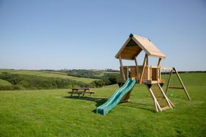 a playground with a slide and a bench in a field at Honeysuckle in Bude