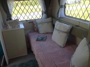 ein kleines Zimmer mit einem Bett mit Kissen und einem Fenster in der Unterkunft KItty unique 60s caravan set in pretty garden in Lizard