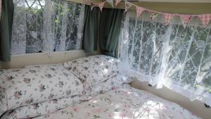 a bedroom with a bed and windows with curtains at KItty unique 60s caravan set in pretty garden in Lizard