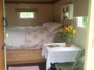a small bedroom with a bed and a table with a vase of flowers at Cosy Shepherds Hut nr Kynance cove in Lizard