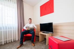a man sitting on a red couch in a living room at Hotel Wanner in Böblingen