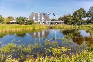 霍勒姆的住宿－Appartement Ut & Thus, Resort Amelander Kaap，一座有两面旗帜的建筑前的池塘