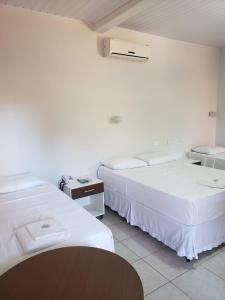 two beds in a room with white walls and a table at Pantanal Hotel in Miranda