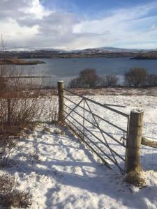 a fence in a snowy field with a body of water at Birdsong Bothy Inviting 1 Bedroom House in Colbost in Colbost