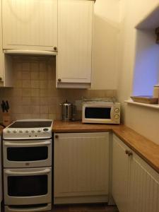 a kitchen with white cabinets and a stove and a microwave at Swallow Barn at Millfields Farm Cottages in Ashbourne