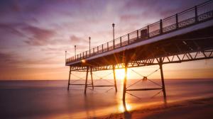 a pier on the beach with the sun setting behind it at Balcony Apartment near Skegness Beach & Town in Skegness