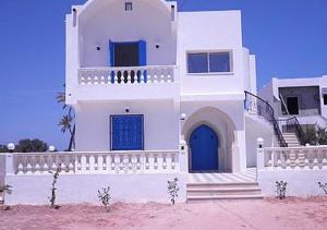 a large white house with a blue door and stairs at 3 bedrooms house at Djerba Midoun 800 m away from the beach with terrace and wifi in Taguermess