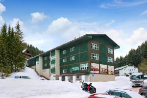 a large green building with cars parked in the snow at Hotel Lenka in Špindlerův Mlýn
