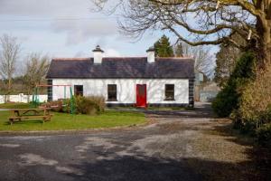 una pequeña casa blanca con una puerta roja en Stunning 3-Bedroom House with Private Garden, en Carracastle