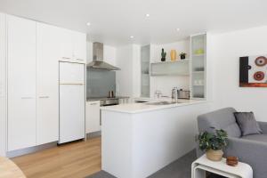 a kitchen with white cabinets and a gray couch at Sunny and Spacious - moments from the Beach and Downtown in Mount Maunganui