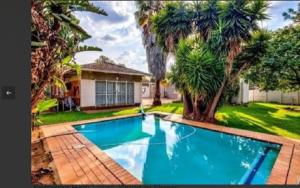 a swimming pool in front of a house with palm trees at Lior-Gil accommodation- in Kempton Park