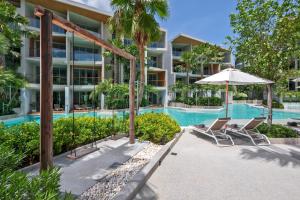 an apartment building with a swimming pool and two chairs and an umbrella at Wyndham Grand Nai Harn Beach Phuket in Nai Harn Beach