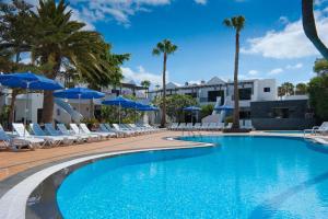 a swimming pool with chairs and blue umbrellas at Apartamentos Fayna in Puerto del Carmen