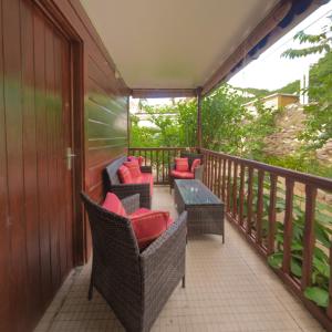 Un balcón con sillas de mimbre y una mesa con almohadas rojas. en Gîtes dans un jardin, en Terre-de-Haut