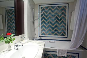 ein Badezimmer mit einem Waschbecken und einer Badewanne mit einem Gemälde an der Wand in der Unterkunft El Mouradi Hammam Bourguiba in Ain Draham