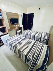 a hotel room with two beds and a television at Hotel Guarumar in Guarujá